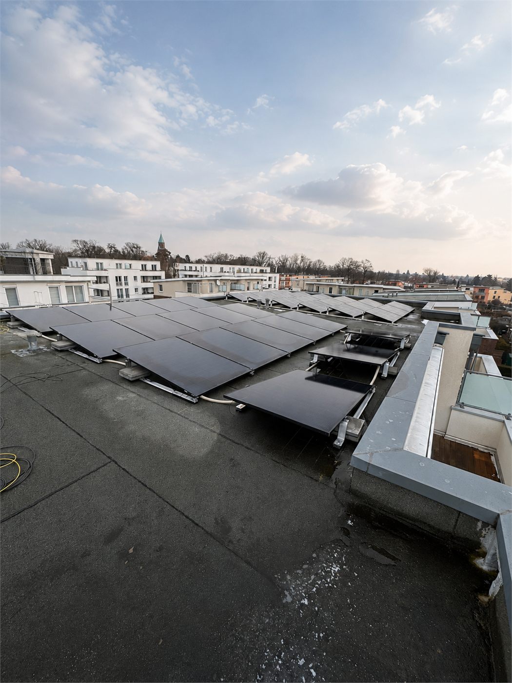 Aufgeständerte schwarze Photovoltaik-Module auf dem Flachdach eines städtischen Mehrfamilienhauses