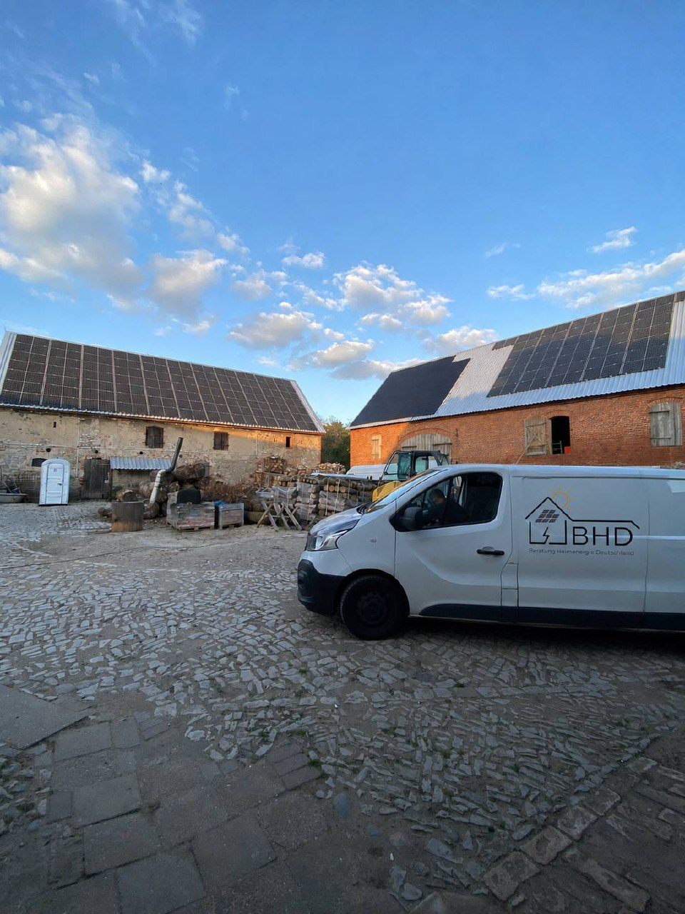 Zwei Scheunendächer eines Hofes vollflächig mit Photovoltaik belegt, davor der Transporter von BHD
