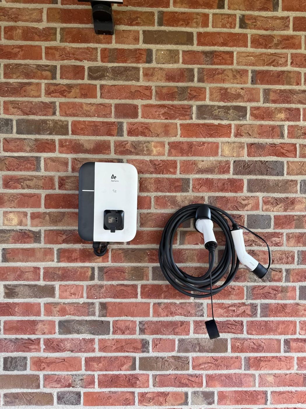 Wallbox mit aufgewickeltem Ladekabel an einer Klinkerwand
