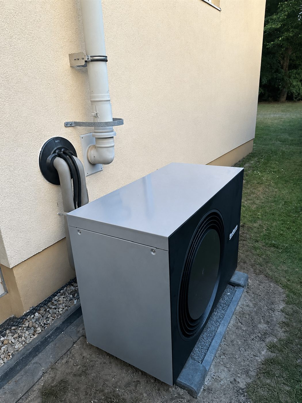 Wärmepumpen-Außengerät auf Betonfundament an der Hauswand im Abendlicht