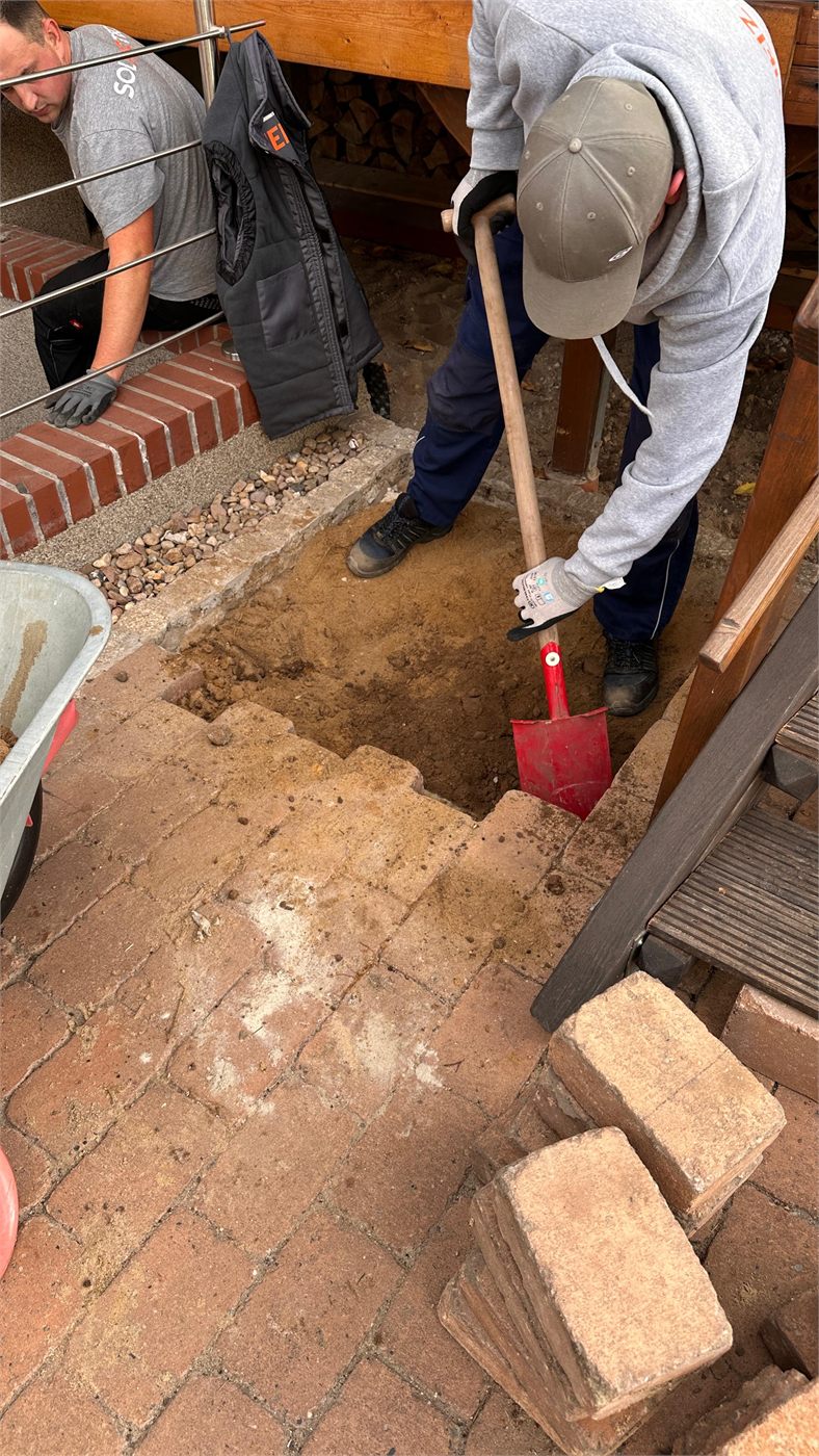 Monteure heben von Hand die Grube für das Fundament der Wärmepumpe im Garten aus
