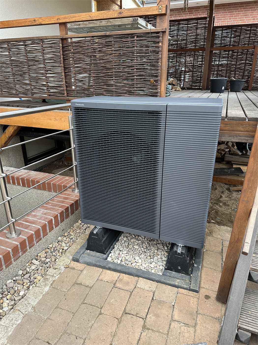 Wärmepumpen-Außengerät auf dem fertigen Fundament neben der Terrasse, Kiesbett darunter