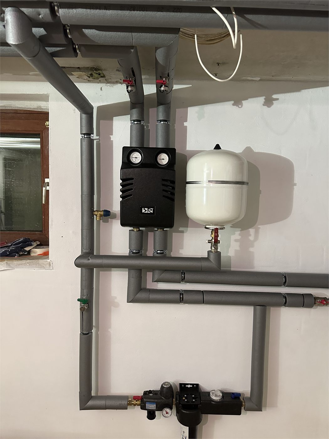 Pumpengruppe mit zwei Manometern, Ausdehnungsgefäß und Systemtrenner an der Kellerwand